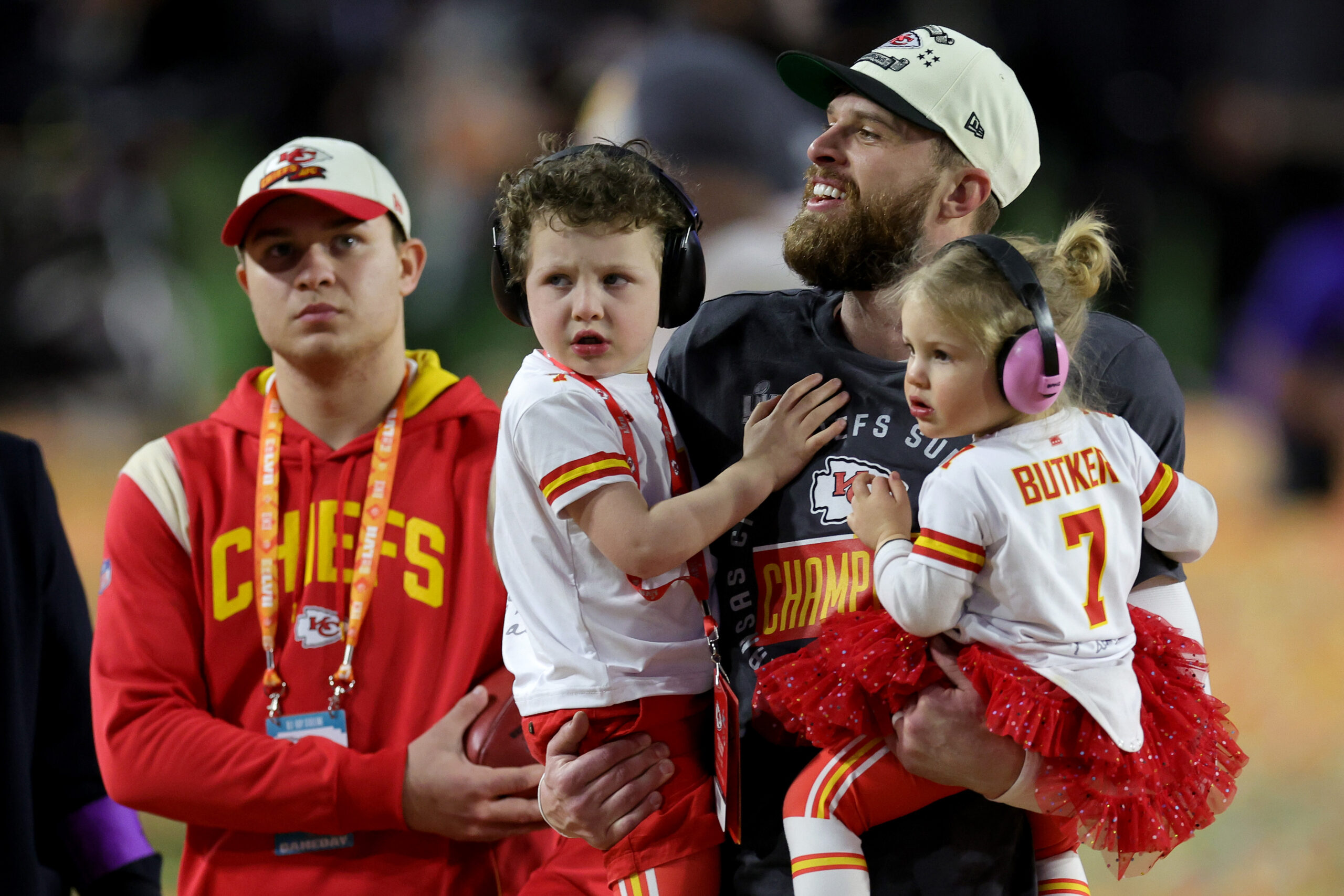 Harrison Butker holding his kids while on a football field.